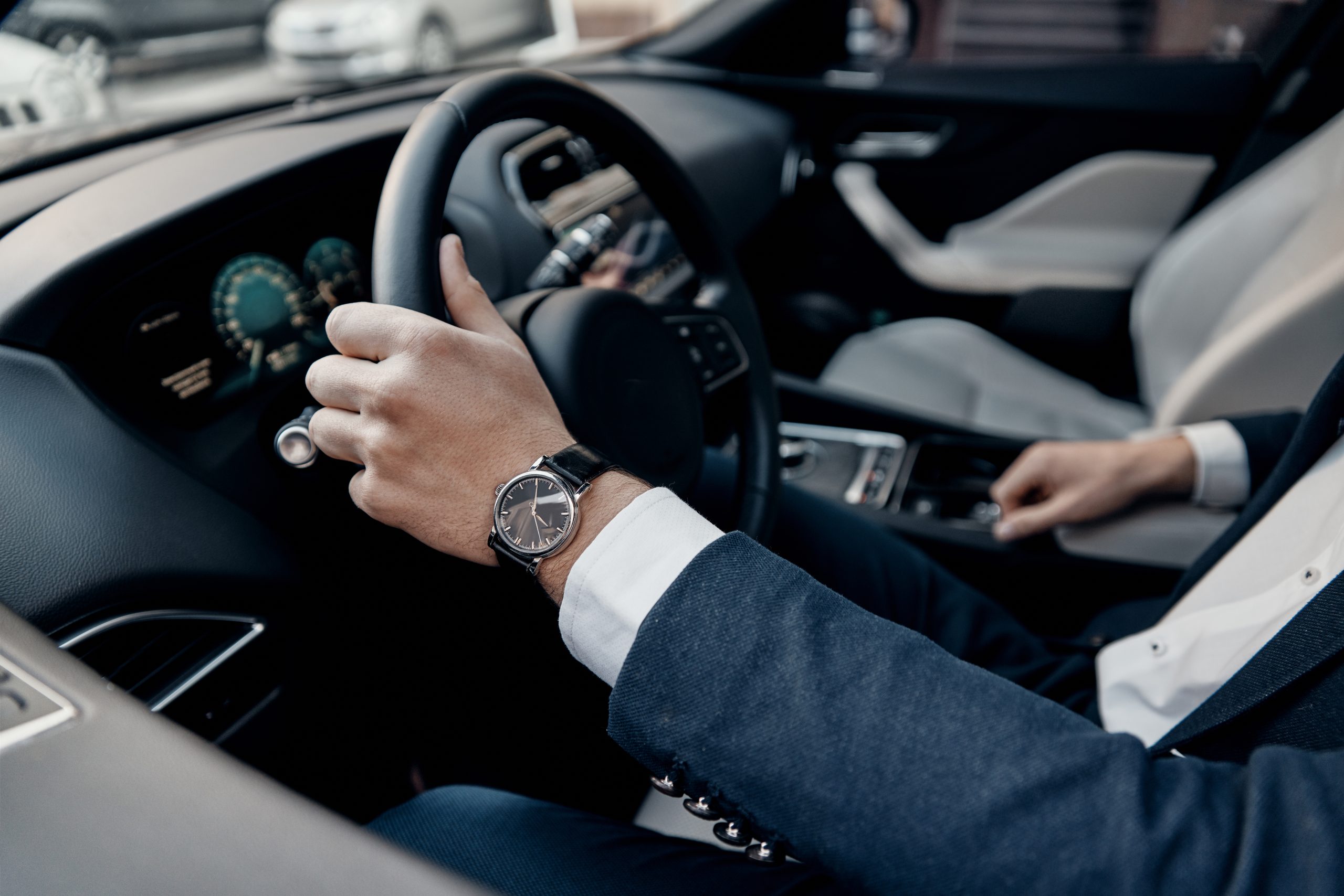 Great car. Close up top view of young man in formalwear keeping hand on the steering wheel while driving a luxury car